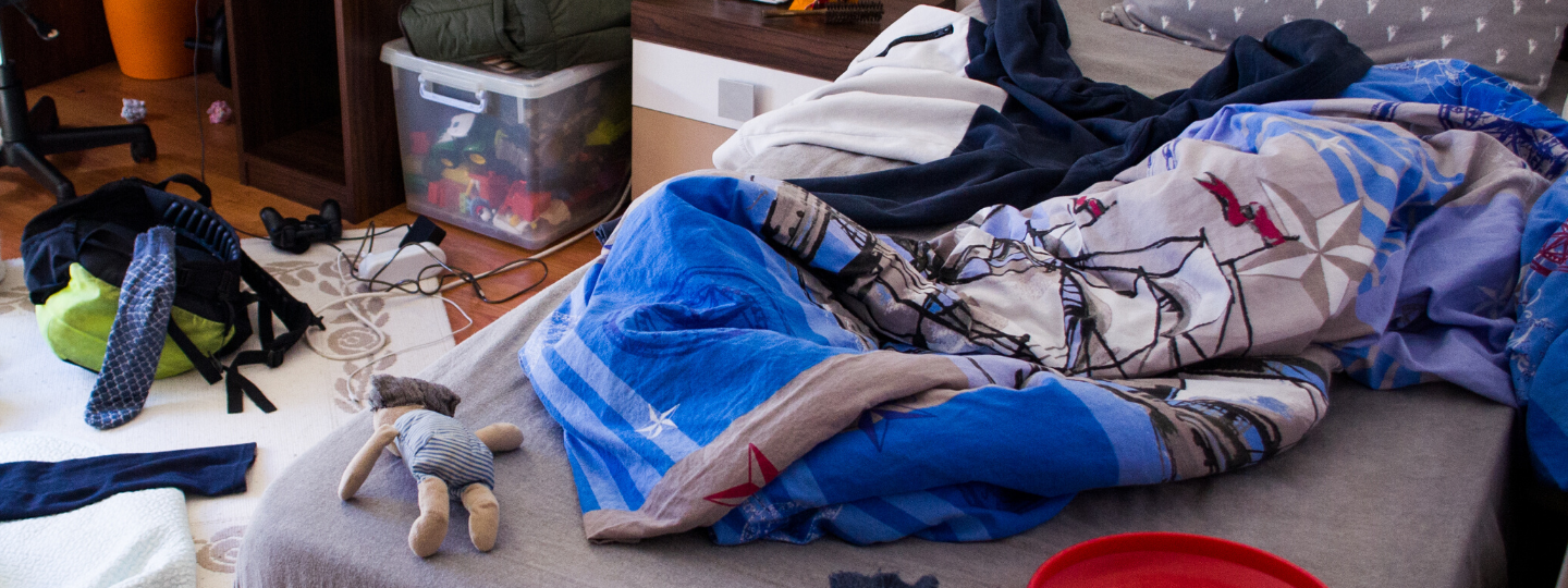 A messy room, focusing on the bed, with blankets all disogranized and junk laying around