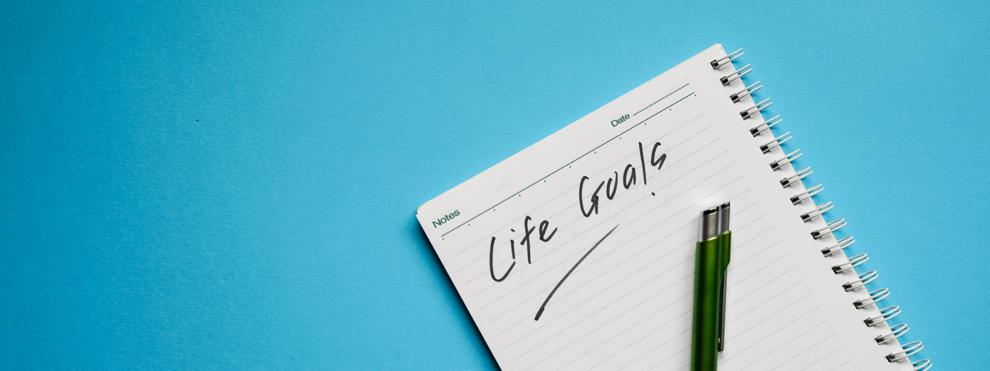A keyboard, post-its and notebook that says 'goals'