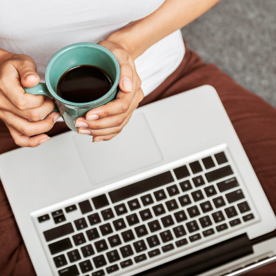 a person holding a cup of coffee at a laptop