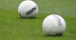Two GAA footballs on a pitch