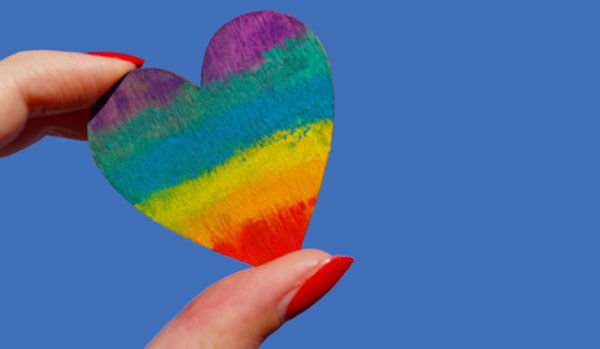 Picture of a rainbow heart held between two fingers