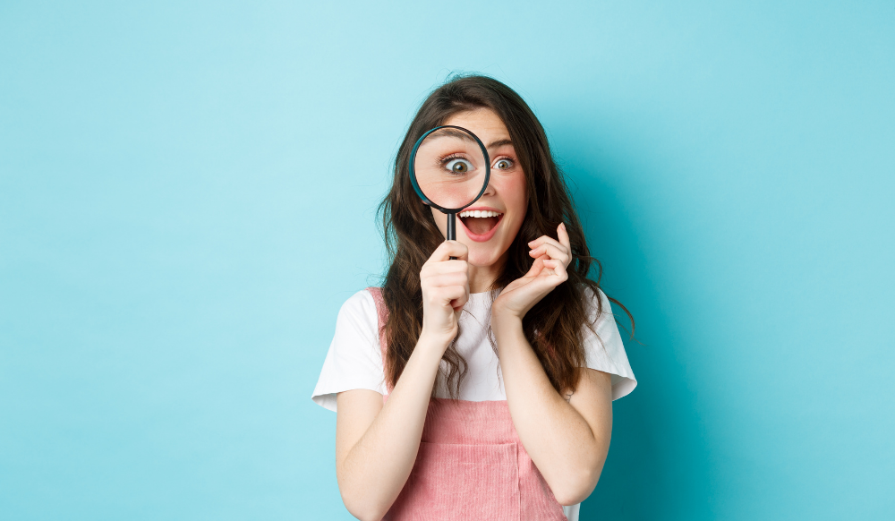 happy young woman looking through magnifying glass
