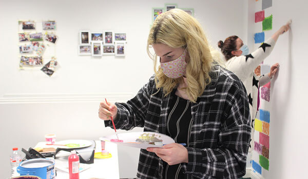 Working in a Jigsaw service A young woman wearing a mask mixes on a paint palette, with another woman working behind her