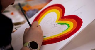 Person painting a colourful love heart on a piece of paper