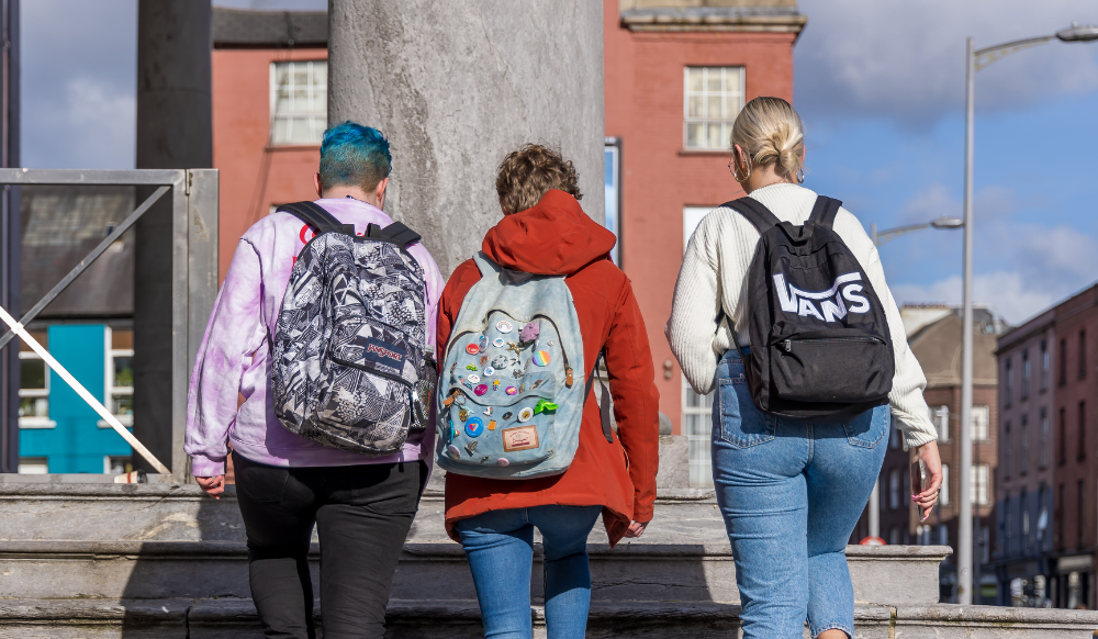three young people wearing backpacks walking away from camera